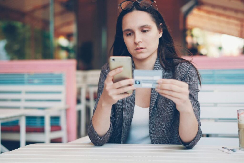 Mulher analisando os gastos da fatura do cartão de crédito pelo celular em um ambiente externo.