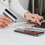 Pessoa segurando cartão de crédito para conferir dados e pagar a fatura do cartão no notebook.