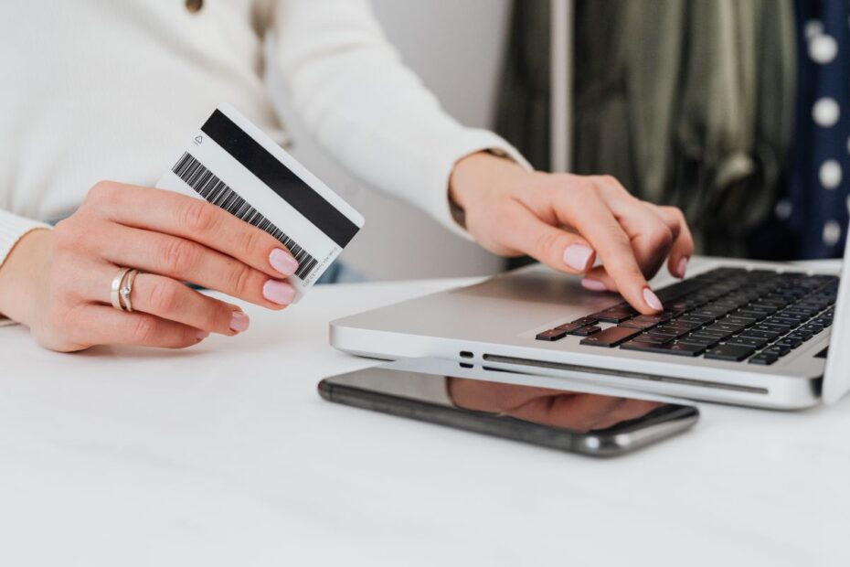 Pessoa segurando cartão de crédito para conferir dados e pagar a fatura do cartão no notebook.